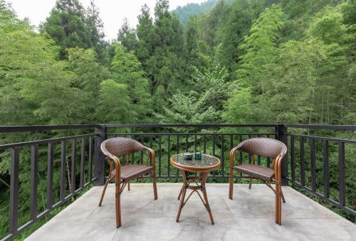 two chairs and a table on a balcony with trees at Zhangjiajie Qiquan Vacation B&B in Zhangjiajie