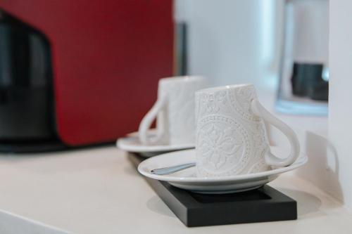 two white cups and saucers sitting on a counter at Casa Luís de Camões - Boutique & Literary House in Santar