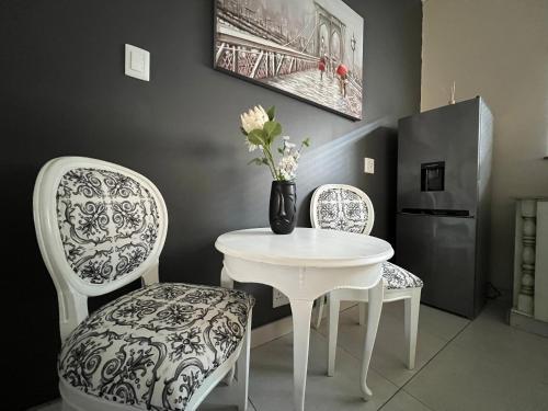 uma mesa branca com duas cadeiras e um vaso com flores em The Lux Guesthouse em Kroonstad