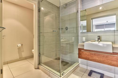W łazience znajduje się szklana kabina prysznicowa i umywalka. w obiekcie Harbour Bridge Waterfront w Kapsztadzie