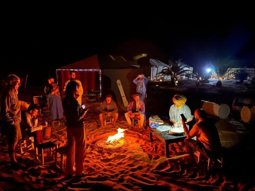 a group of people sitting around a fire on the beach at Camel Luxury Camp in Merzouga