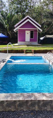 a swimming pool with a purple house in the background at Teniat Village in Rantau Panjang