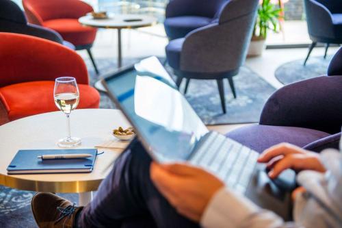 a person sitting at a table with a laptop and a glass of wine at Best Western Hotel Atlantys Zenith Nantes in Saint-Herblain