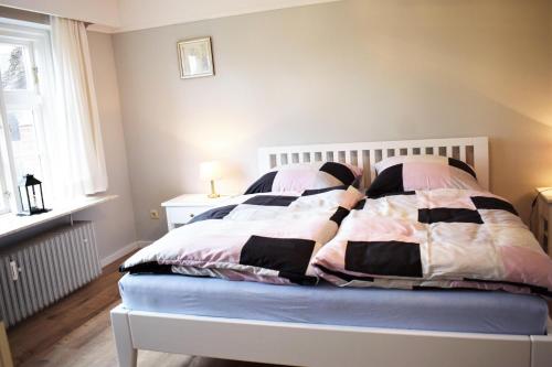 Cama blanca con mantas y almohadas rosas y negras en Haus Amsel, en Niebüll