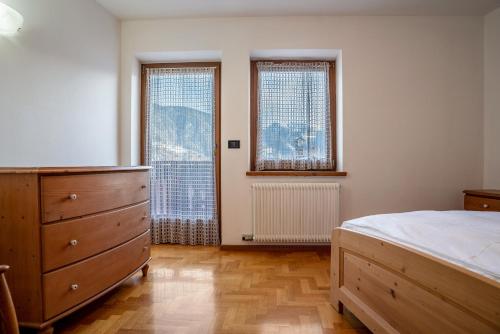 a bedroom with a bed and a dresser and two windows at Casa al portico Val di Cembra in Grauno