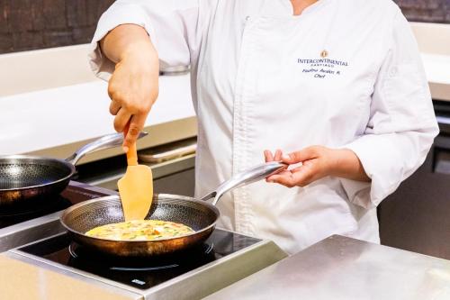 a chef cooking food in a pan on a stove at InterContinental Santiago by IHG in Santiago