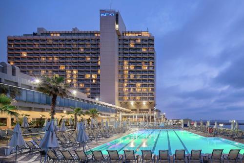a large swimming pool with chairs and a building at Hilton Tel Aviv Hotel in Tel Aviv