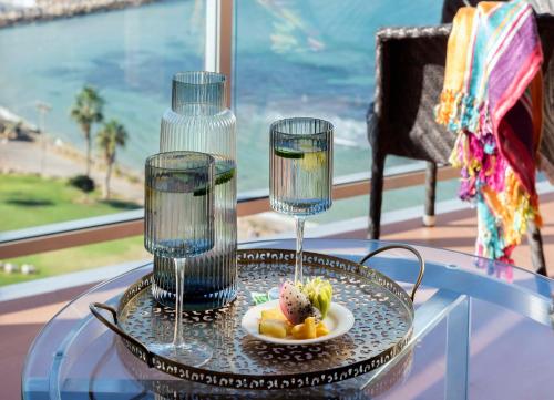 a glass table with a plate of food and two wine glasses at Hilton Tel Aviv Hotel in Tel Aviv