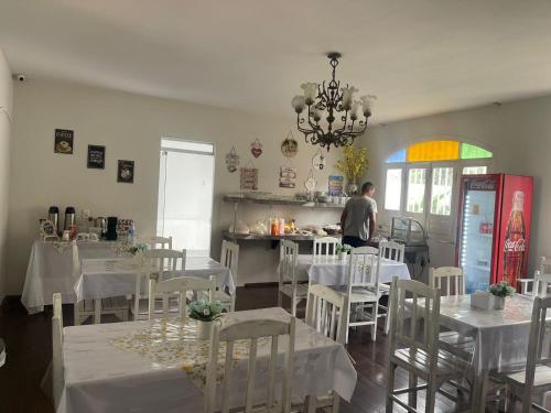 um restaurante com mesas e cadeiras brancas e um homem na cozinha em POUSADA FLOR DO IPÊ em Juazeiro do Norte