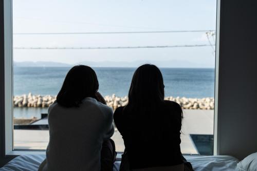 two women sitting on a bed looking out of a window at ヴィランス淡路島 in Sumoto