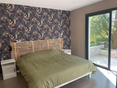 Schlafzimmer mit einem grünen Bett und einem großen Fenster in der Unterkunft La Villa de la Pinède in Langlade