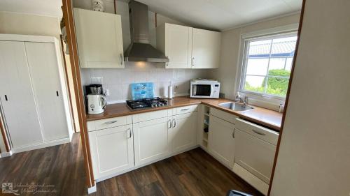 a kitchen with white cabinets and a sink and a microwave at Chalet 128 Krabbenkreek in Sint Annaland