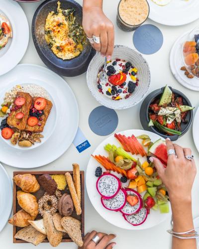 a table full of plates of food with people reaching for food at DeLight Boutique Hotel - Small Luxury Hotels of the World in Agios Ioannis Mykonos