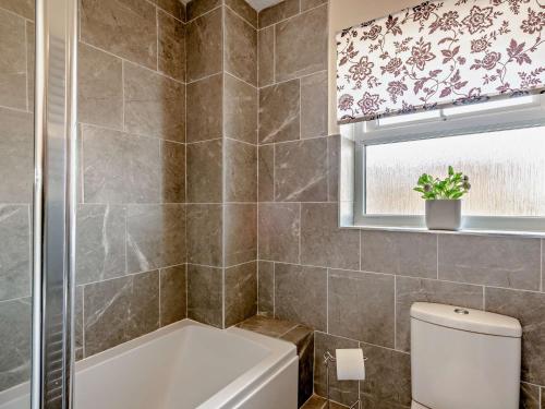 a bathroom with a tub and a toilet and a window at 3 Bed in Sheringham 43467 in Sheringham