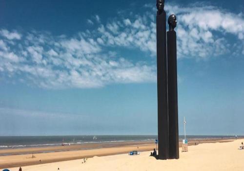 a large black pole on a beach with the ocean at Hotel Maxim in De Panne