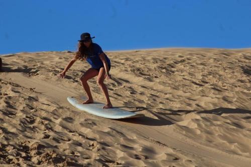 a woman standing on a surfboard in the sand at TRAVEL SURF NATURE in Tamraght Ouzdar