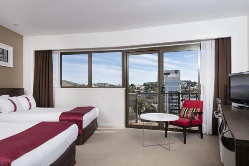a hotel room with two beds and a table and a tv at Hotel Grand Chancellor Townsville in Townsville