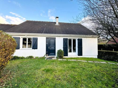 a white house with a black door on a yard at Maison rénovée et chaleureuse proche du mémorial in Caen