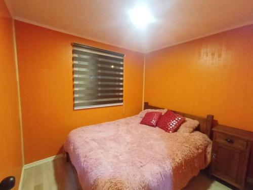 a bedroom with orange walls and a bed with red pillows at Los Dálmatas in Osorno