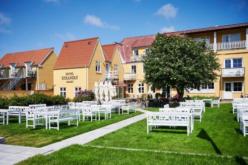 une pelouse avec des tables et des chaises blanches devant un bâtiment dans l'établissement Hotel Strandly Skagen, à Skagen
