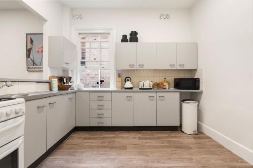 a white kitchen with white cabinets and a wooden floor at Stunning Terraced Apartment near the Sydney Opera House in Sydney