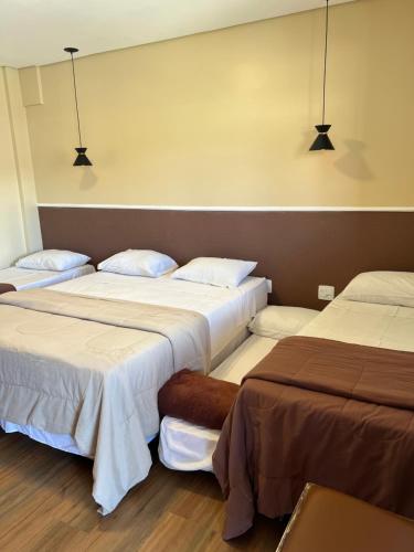 three beds in a hotel room with lights on the wall at Rogai Hotel Pousada in Aparecida