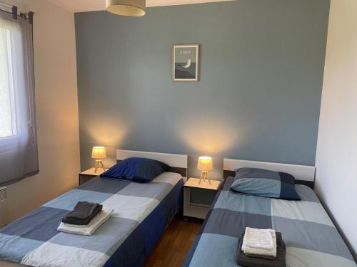 two beds in a room with two lamps and towels on them at La petite maison in Quemper-Guézennec