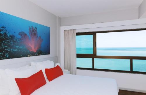 a bedroom with a bed with red pillows and a window at Hotel Ponta Verde Maceió in Maceió