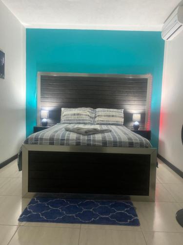 ein Schlafzimmer mit einem schwarzen Bett und einer blauen Wand in der Unterkunft Beautiful 3-Bed House in Saint Catherine Portmore in Central Village