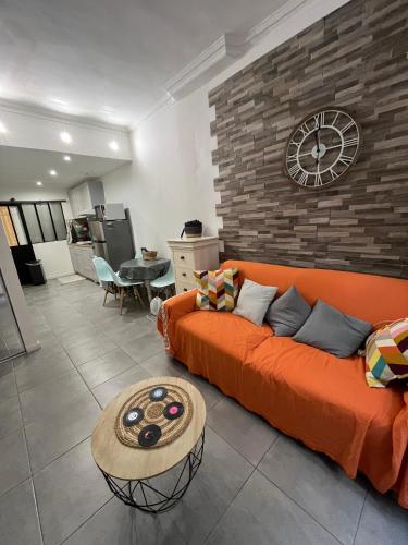 - un canapé orange dans un salon avec une horloge murale dans l'établissement perle rare à la ciotat, à La Ciotat