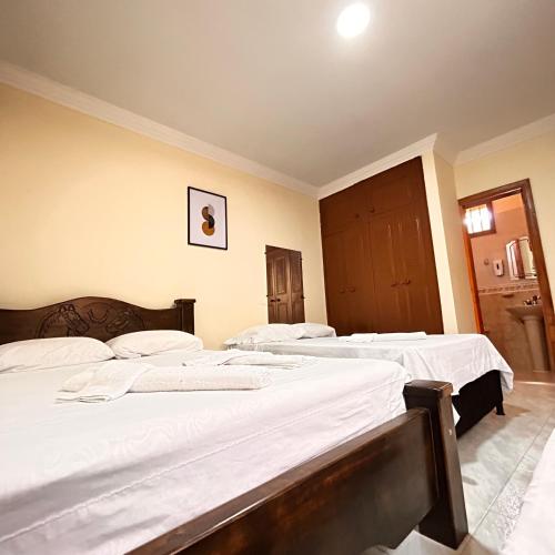 two beds in a bedroom with white sheets at Casa Hotel Los Fundadores in La Victoria