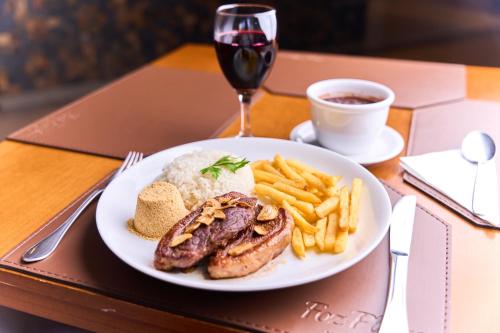 a plate of food with meat and rice and a glass of wine at Foz Plaza Hotel in Foz do Iguaçu