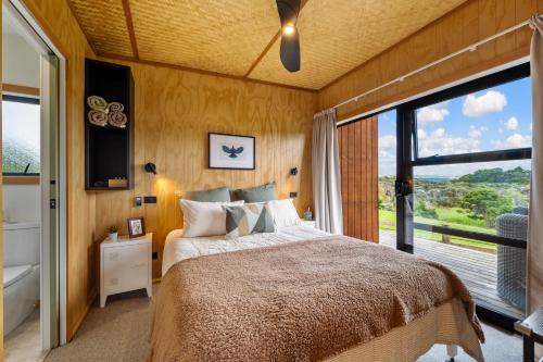a bedroom with a large bed and a large window at Kūkū Kabin - Waimate North Eco Holiday Cabin in Kerikeri