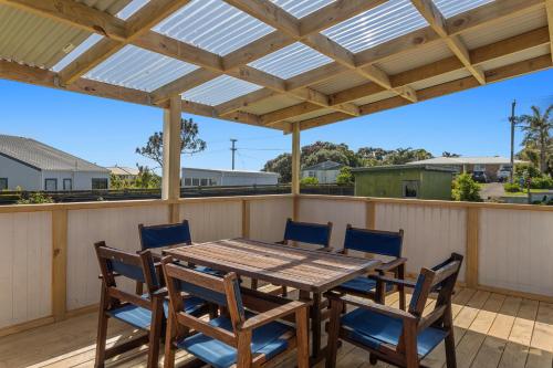 a wooden table and chairs on a deck with a pergola at Back to the Beach Bach in Waiotahi