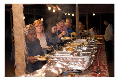 een groep mensen die bij een buffet staan met eten bij Luxury Overnight stay in Desert Safari Campsite, with dinner, adventure, entertainments, and transfers in Dubai