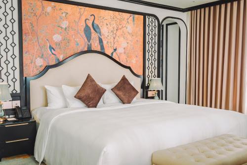 a bedroom with a white bed with a painting on the wall at La Vela Hue Hotel in Hue