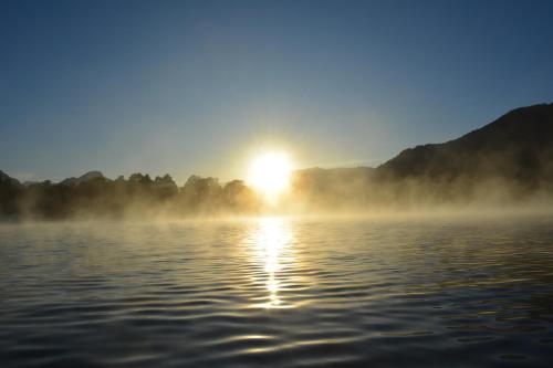 a misty lake with the sun in the background at Casa en Choshuenco a 180 metros de la Playa, Panguipulli, Los Ríos in Panguipulli