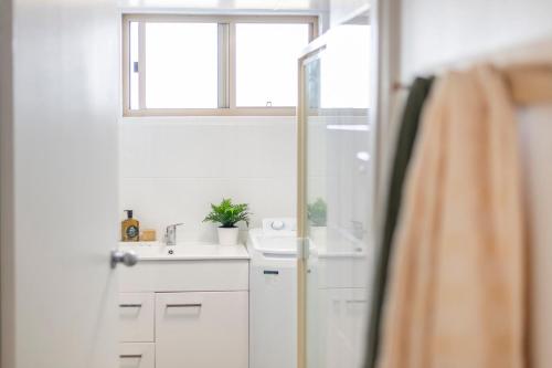 a white bathroom with a sink and a window at Poppy's Place - oceanstays in Yamba