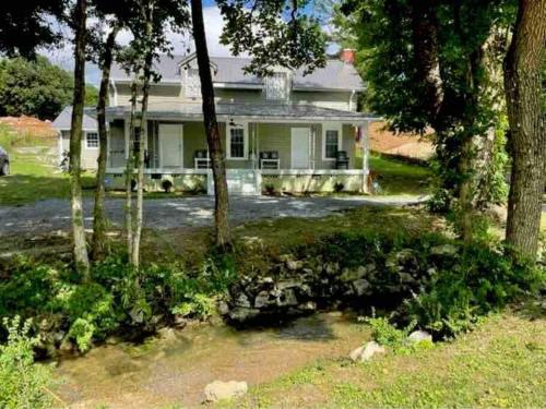 a white house with trees in front of it at Farmhouse with game room, fire pit and creek in Johnson City