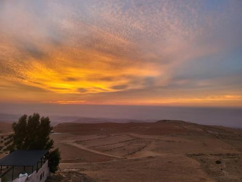a sunset over the desert with a building on a hill at Al Namteh Lodge in ‘Ābil