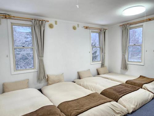a row of beds in a room with windows at guest house White House ホワイト ハウス in Shimukappu