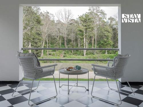 two chairs and a table in front of a window at The Mudra Manor 4BR Coorg temperature controlled pool Villa in Madikeri