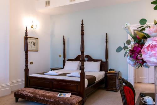 a bedroom with a canopy bed with a bench and flowers at Keppels Head Hotel in Portsmouth