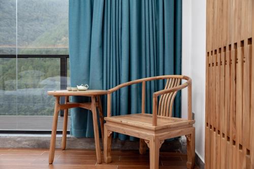 a wooden chair and a table in front of a window at Zhangjiajie Qiquan Vacation B&B in Zhangjiajie