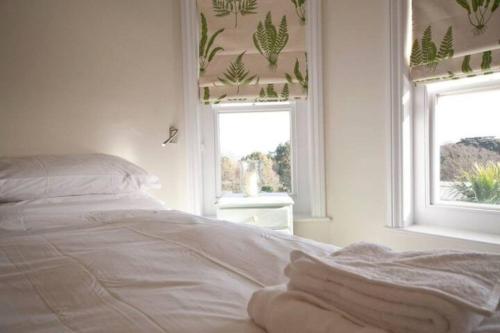 a bedroom with a white bed with two windows at Signal Point Cottage in Ventnor