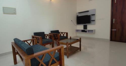 a living room with chairs and a table and a tv at Hobiz Serviced Apartments Chalakuzhy Nr Medical College Trivandrum in Trivandrum