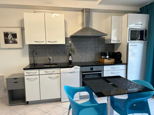 une cuisine avec des placards blancs et une table avec des chaises bleues dans l'établissement Village naturiste - Port-Nature 7 - Le Maryline - 3ème étage - vue Port, au Cap d'Agde
