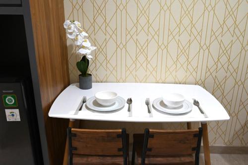 a white table with two plates and a vase of flowers at Apartment Medan Podomoro City Deli by OLS Studio in Medan