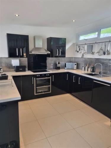 a large kitchen with black cabinets and white tile floors at BRANTLEA Detached 4 Bed Home, Hot Tub, Lake View, Parking, Pet Friendly in Bowness-on-Windermere