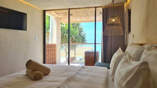 a bedroom with a white bed with a large window at Shore Thing Gili Air Beachfront Apartment in Gili Air